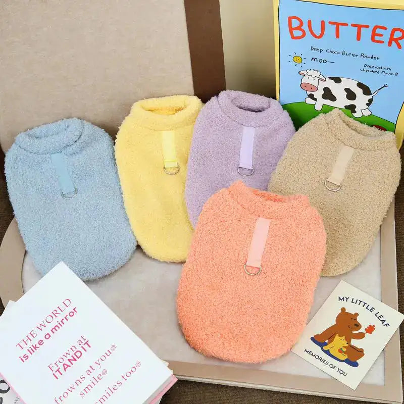 Five colorful dog sweaters on a box with books underneath.