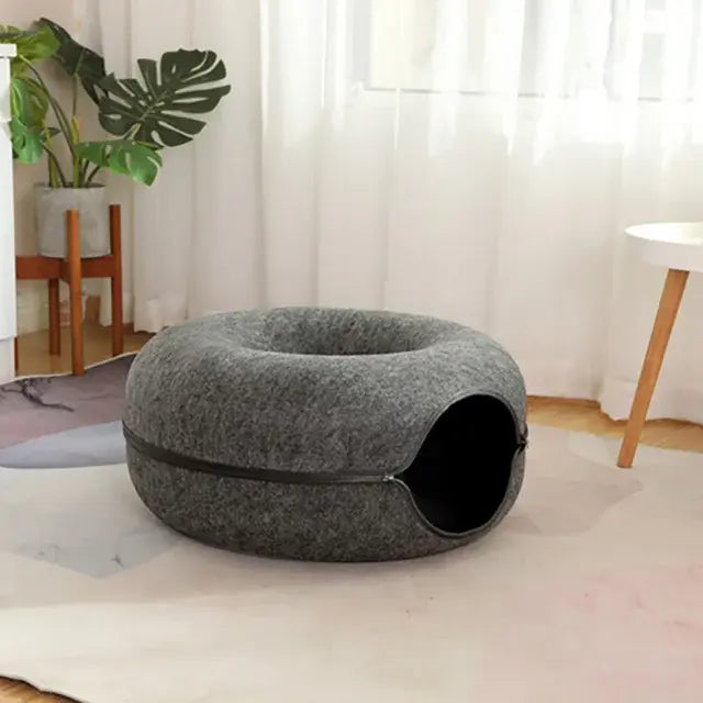 Gray pet bed on a white floor with a plant and curtain in the background