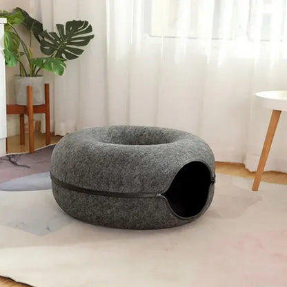 Gray pet bed on a white floor with a plant and curtain in the background