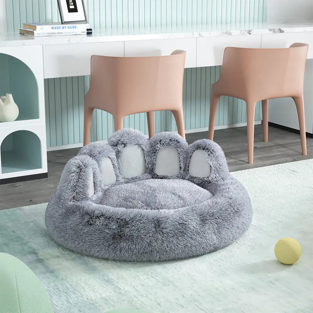 Gray paw-shaped pet bed on a light wooden floor with a modern interior background.